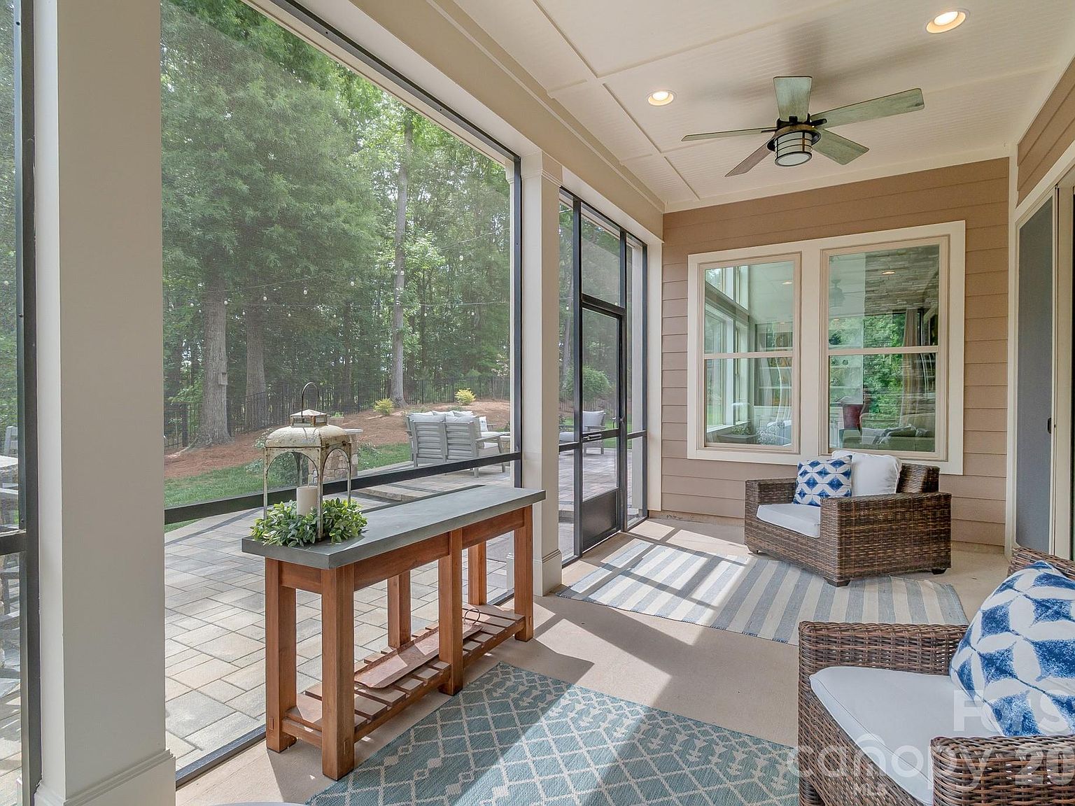 The screened porch. Covered ceiling, wicker seating, view through screens to the patio and pines beyond.