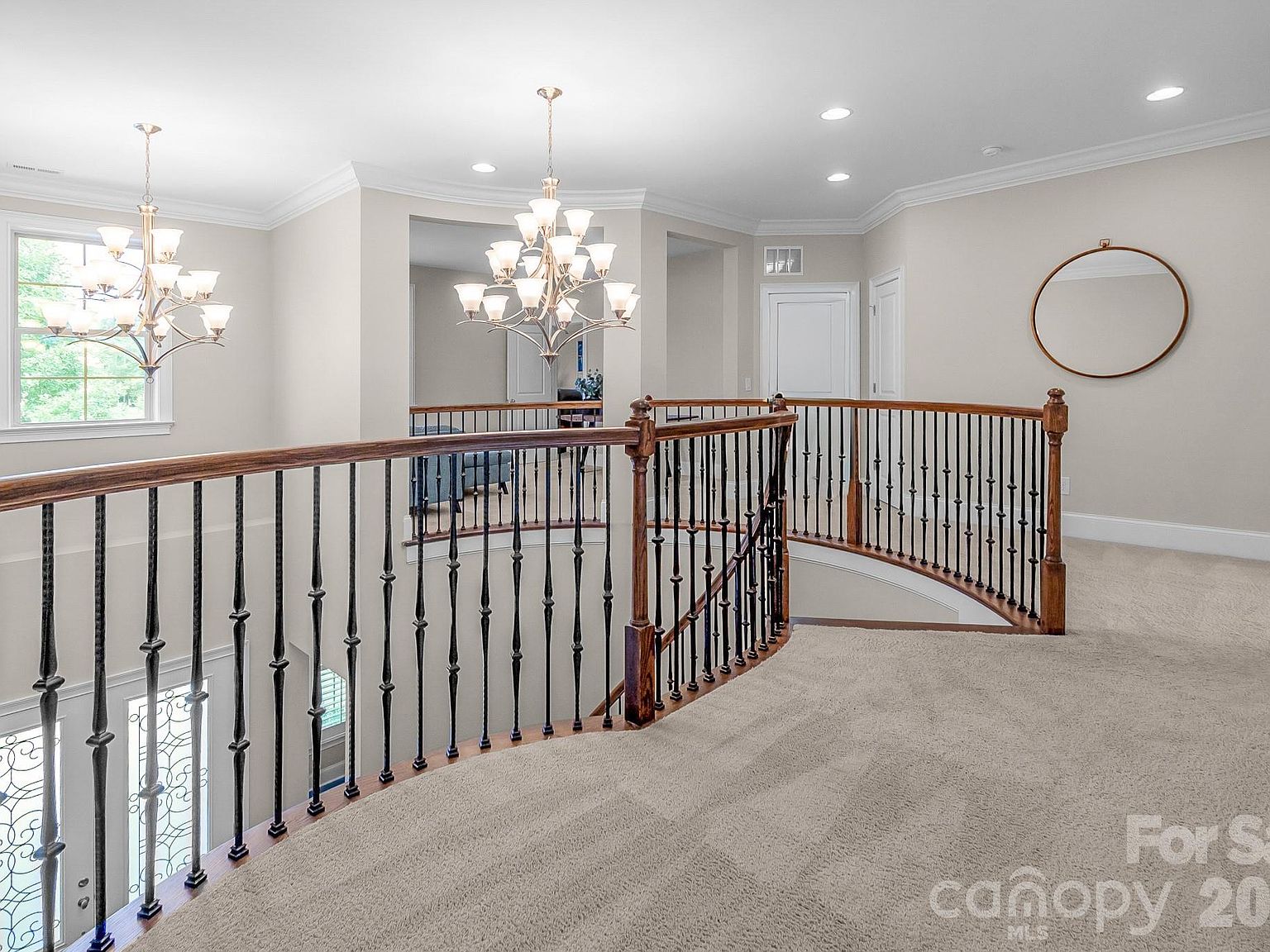 Upstairs landing: curved railing with iron balusters overlooking the foyer below, twin chandeliers, hallway to the additional bedrooms.