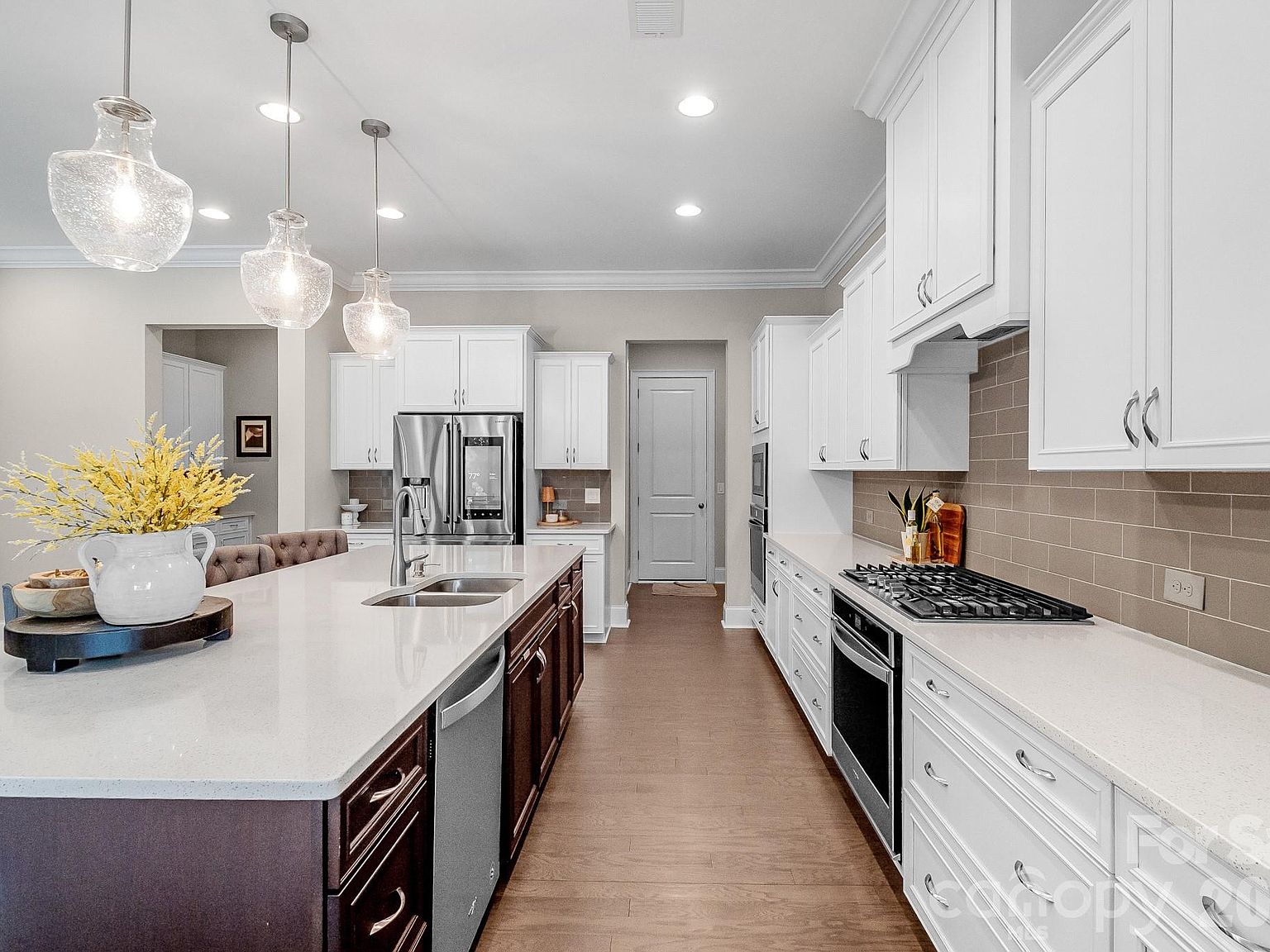 The kitchen looking down the prep run: pendant lighting, quartz waterfall island, stainless gas range and double oven.