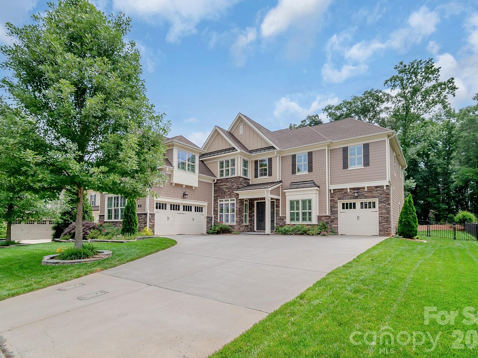 Front elevation of 421 Vintage Creek Dr. A stone-and-shingle transitional Craftsman with double gables, two garages, and a manicured lawn set against tall trees.